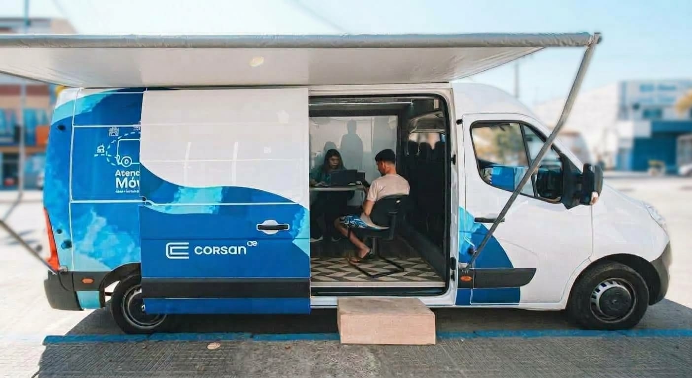 Van de atendimento móvel da Corsan estacionada, com toldo aberto e um atendente sentado em seu interior.